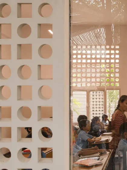 A detail shot looking through a window into a classroom at the rural school. The layers of jaali screens and bamboo roofing create a rich texture and a gentle, diffused light that is ideal for a learning environment.
