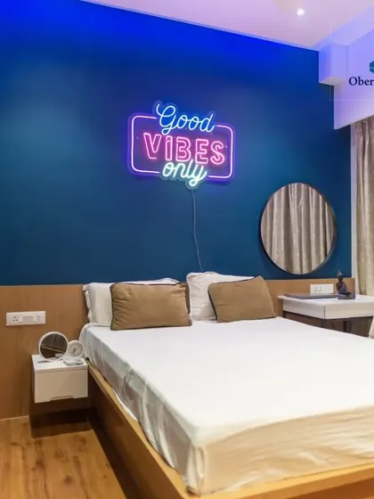 A full view of this modern bedroom, featuring a bold blue accent wall and a "Good Vibes Only" neon sign. Our custom bed with a simple wooden frame and floating side table completes the contemporary look.
