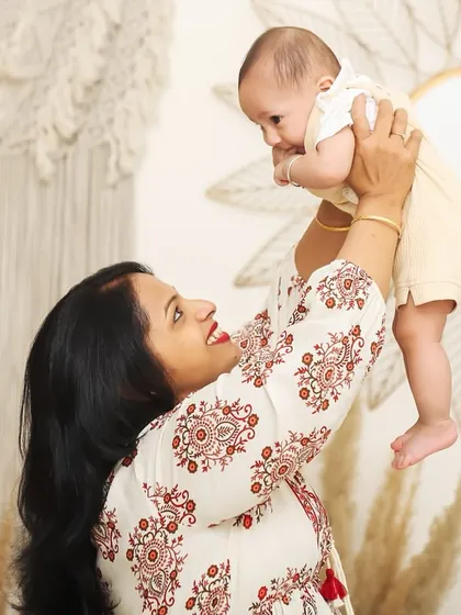 A mother lifts her baby high in the air, both of them smiling. This candid shot in the studio captures a moment of pure, unscripted joy.