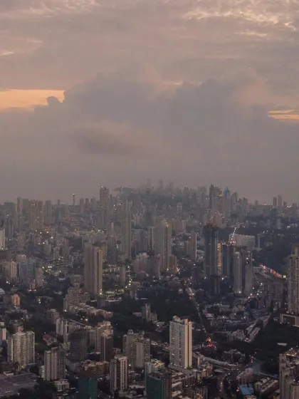 A drone's view looking down on the dense urban fabric of Mumbai, with clouds gathering over the city.