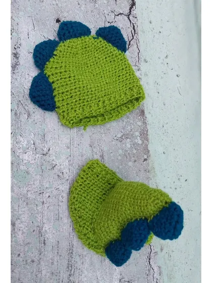 A detailed product shot of my handmade dinosaur outfit. You can see the texture of the yarn and the construction of the blue spikes on the lime green hat and diaper cover.
