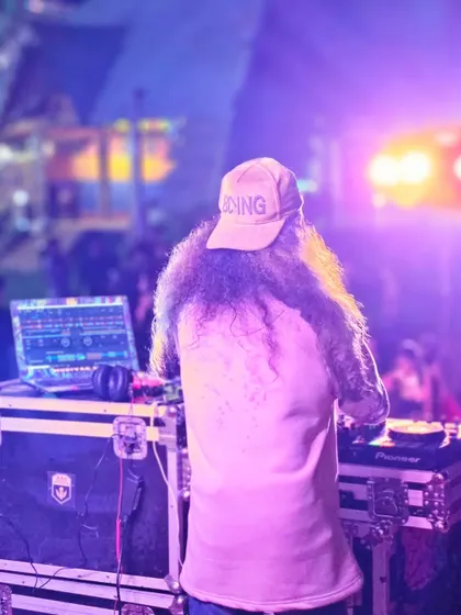 A view from behind, showing me at the decks during a festival, with the crowd and lights blurred in the background.