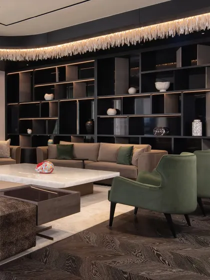This living space features a large, comfortable sofa set against a dark, expansive bookshelf. The green armchairs add a touch of color, while the white marble coffee table provides a bright contrast.