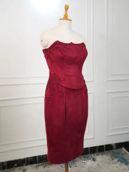 A full view of the red suede corset dress on a mannequin, showcasing its form-fitting shape and the placement of the signature creeper embroidery.