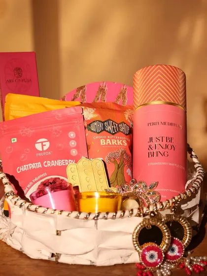 A close-up of the pink-themed Diwali hamper, showing the details of the goodies inside, including a "Just Be & Enjoy Being" perfume mist.