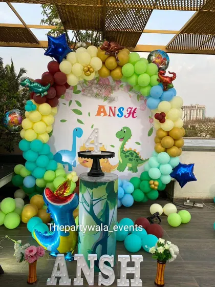 A roaring good time with a dinosaur theme for a 4th birthday. This outdoor setup features multiple dinosaur cutouts and a colorful balloon arch.