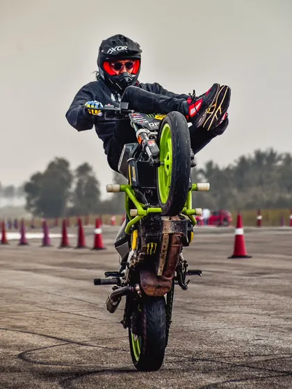 A rider executes a "high chair" wheelie, sitting on the handlebars while the bike is on one wheel. This is an advanced stunt that requires incredible core strength and balance.
