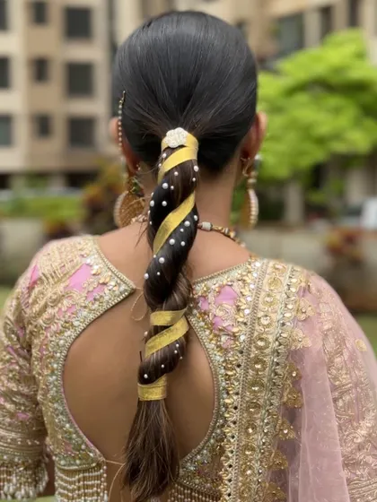 A sleek and modern twisted braid, wrapped with a golden ribbon and dotted with pearls. This is a chic and stylish option for a festive occasion or pre-wedding event.