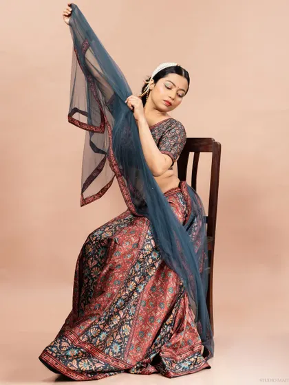 A model seated gracefully in a printed lehenga, using the sheer dupatta to create a sense of movement and elegance. This is a beautiful shot for an ethnic wear catalogue.