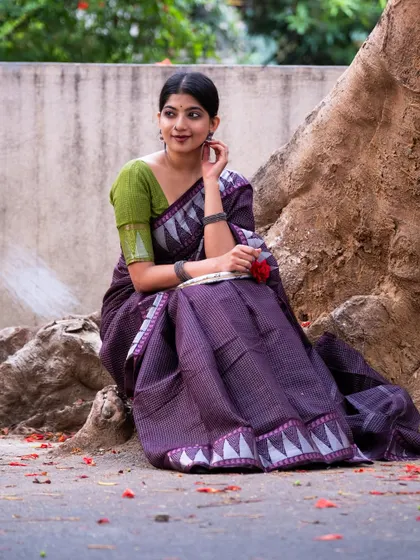 Modeling a purple Sungudi cotton saree with a unique temple border design. The shot is framed to highlight the texture of the fabric and the elegant way it sits.