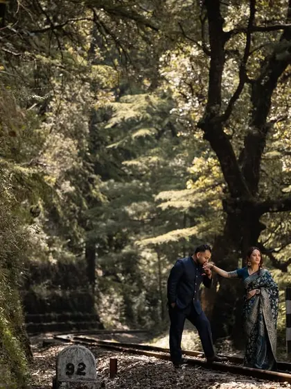 A gentlemanly kiss on the hand along the forested railway tracks. The soft, filtered light through the trees creates a dreamy, romantic atmosphere.