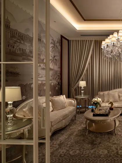 Every detail in this living room, from the vintage wallpaper depicting a classical landscape to the crystal chandelier, speaks of timeless elegance. This space, part of The Ivory Royale, is designed for those who appreciate the finer things in life.