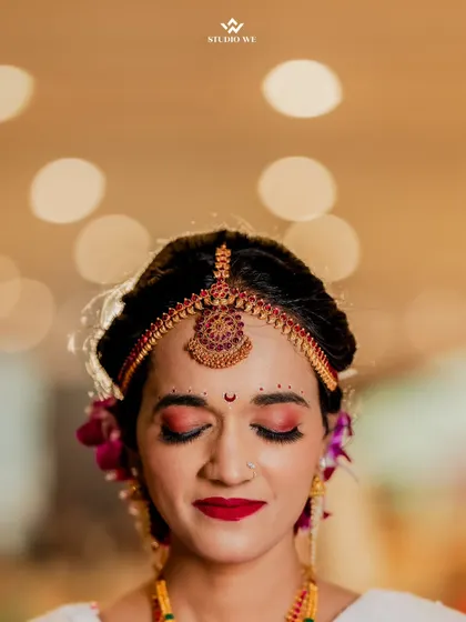 A close-up of the bride's face, her eyes closed, highlighting her beautiful makeup and traditional maang tikka.