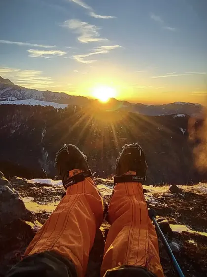 A first-person view of a trekker's boots and the stunning sunrise over the snow-clad mountains. This is the peaceful, golden moment you wake up to on our high-altitude winter treks.