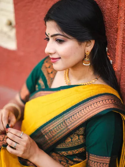 A close-up shot of a yellow saree with a dark green border, focusing on the intricate details of the fabric and the traditional gold jhumkas that complete the look.