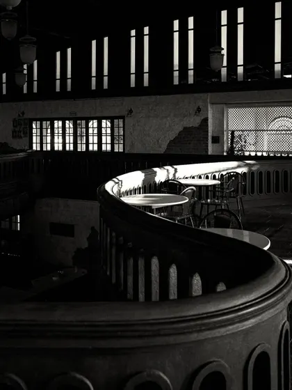 Sunlight filtering through the narrow upper windows creates stripes of light across the dark, curved balcony, highlighting its form.