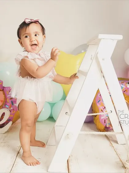 Standing tall and proud next to a prop ladder, this birthday girl is ready to climb and explore. A great shot showing off her new standing skills.