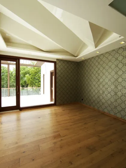 The Cards Room at Sachdeva Farmhouse is a refined leisure space with warm wooden flooring and elegant patterned wallpaper. A striking geometric ceiling and large glass doors connect the room to the terrace.