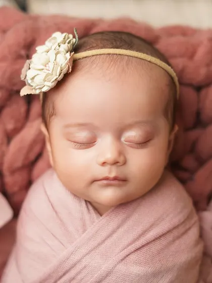 A tight close-up of the sleeping newborn's face, showing the delicate details of her floral headband and the soft texture of the wrap.
