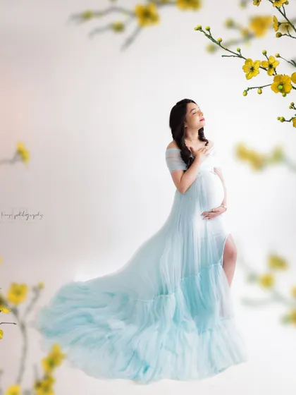 A moment of pure bliss. This mama-to-be looks up, lost in a happy thought, surrounded by a cloud of light blue tulle and delicate flowers.