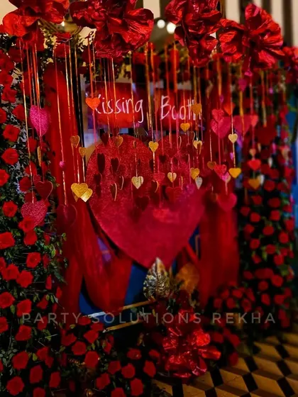A fun and romantic "Kissing Booth" photo corner. The backdrop is lavishly decorated with red roses, hanging hearts, and dramatic lighting, creating a playful and intimate spot for couples.