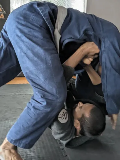 Jiu-Jitsu is an obsession, and we're here for it. A student works on a pass during a live roll, showcasing the dynamic nature of Gi grappling.