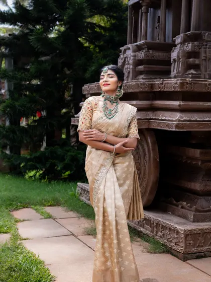 A full-length shot of the cream and gold silk saree against a historic temple backdrop. This shows how the outfit is perfect for a traditional and grand pre-wedding photoshoot.
