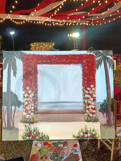 My easel set up at the Goa wedding venue. The canvas shows the background of the red floral arch and the sea, painted before the couple's ceremony began.