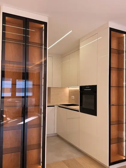 A perspective shot of the modern white kitchen, showing the seamless integration of the built-in oven and the beautiful contrast of the wood-grain interior of the display cabinets.
