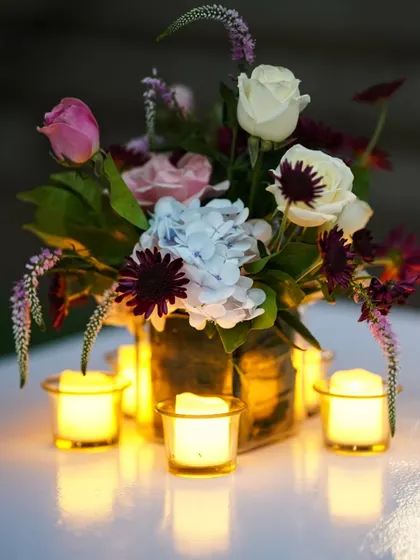 It's the little details that create magic. A close-up of a table centerpiece featuring a mix of beautiful flowers surrounded by the warm, flickering glow of candles, adding a touch of romance to the evening.