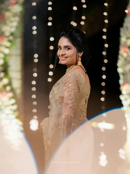 A beautiful portrait of a guest or bride, her golden saree shimmering against the bokeh of the reception lights.
