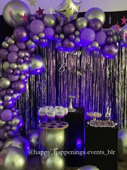 A wide-angle view of a purple and silver party setup. The balloon arch frames the space beautifully, creating an inviting area for photos and celebration.