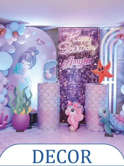 A complete mermaid-themed decor setup for a birthday party. This backdrop includes a shimmering sequin panel, a neon "Happy Birthday" sign, and adorable sea creature props to create a perfect underwater photo zone.