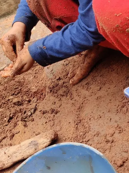 A child explores the texture of wet sand, discovering its properties through hands-on, self-directed play.