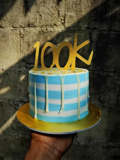 A cake to celebrate a 100k follower milestone. The blue and white striped buttercream with a white drip is a clean and celebratory design.