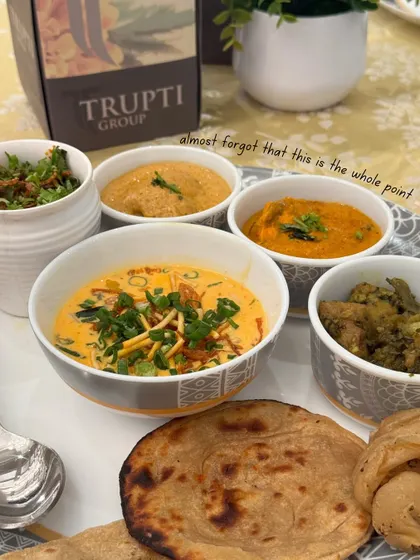A beautifully arranged plate of traditional Indian food, featuring various curries, dal, and freshly made roti, with our Trupti Group branding in the background.