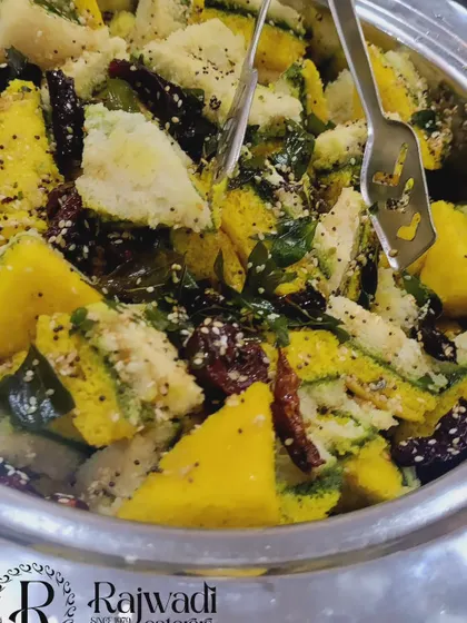 A close-up of my Gujarati Khaman Dhokla. It's soft, spongy, and tempered with mustard seeds, curry leaves, and sesame, served in a traditional steel serving bowl.