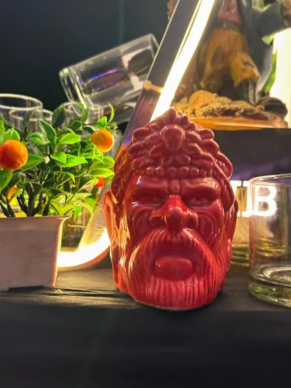 A vibrant red tiki-style mug, adding a pop of color and personality to the bar setup.