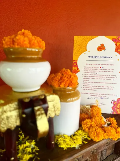 A fun and creative "wedding contract" sign, styled with traditional pickle jars (bharanis) and marigold flowers.