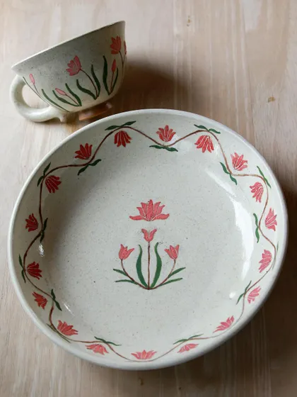 A hand-painted plate and cup set from the 'Gul' collection. The vibrant red and pink florals bring a touch of nature's beauty to the dining table.