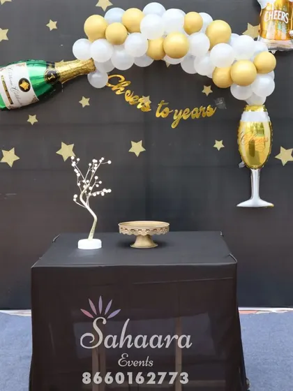 "Cheers to the years!" This fun bachelor party or milestone birthday backdrop features a champagne bottle balloon, a starry night theme, and a table for cake and gifts.