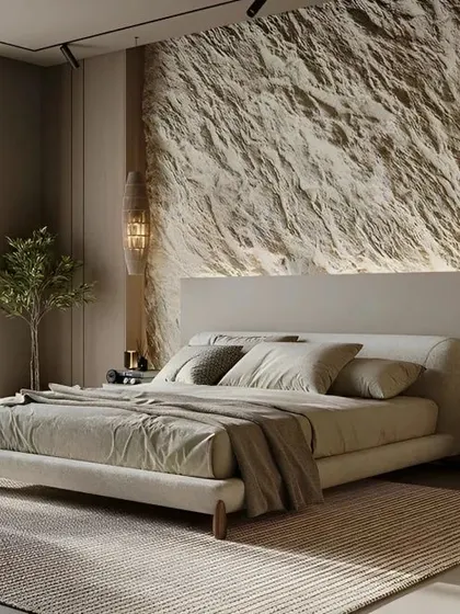 This bedroom design brings natural elements indoors with a stunning stone-textured accent wall. The warm, diffused lighting enhances the texture, creating a calm, earthy, and organic feel.