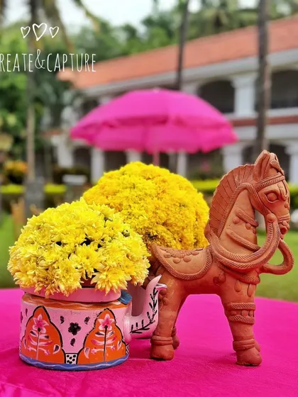 A quirky and colorful table centerpiece for a Mehendi, featuring a painted pot, a terracotta horse, and bright yellow flowers.