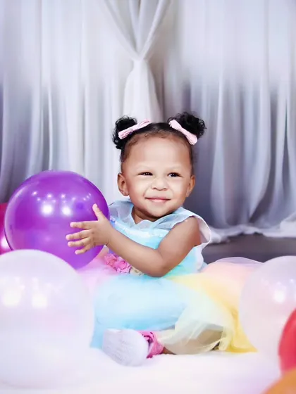 A sweet moment with a one-year-old girl hugging a purple balloon during her birthday photoshoot.