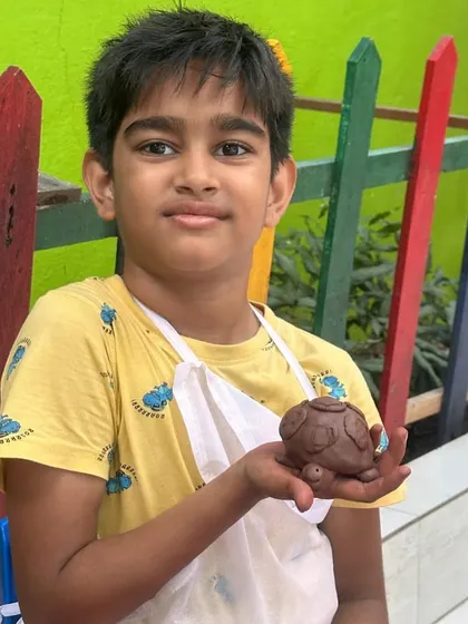 A proud student displays his finished clay turtle. This moment captures the sense of accomplishment children feel when they hold a tangible result of their imagination and effort.