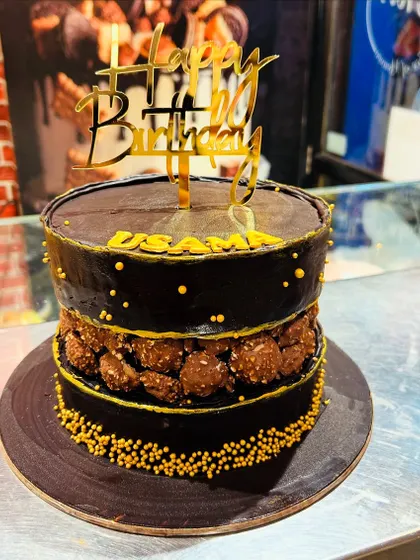 A decadent chocolate cake with a fault line filled with Ferrero Rocher chocolates, topped with a gold "Happy Birthday" sign.