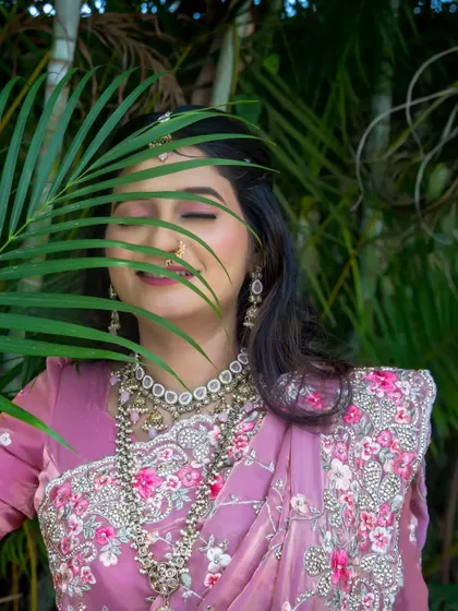 An artistic bridal portrait with a palm leaf creating a natural frame, her eyes closed in a moment of blissful happiness.