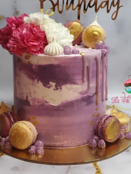 I call this my "lavender haze" cake. It features a purple marble buttercream effect, a rich purple drip, and is decorated with macarons and fresh flowers.