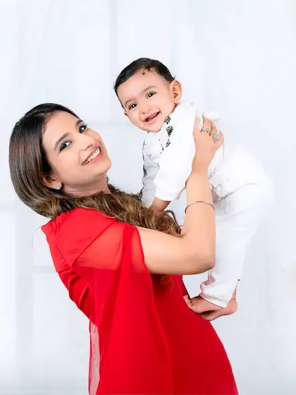 A mother in a beautiful red gown lifts her smiling baby high. The joy and love in this moment are palpable.