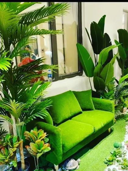 This cozy corner is filled with various artificial tropical plants, including palms and birds of paradise, surrounding a bright green sofa to create a lush, indoor jungle vibe.